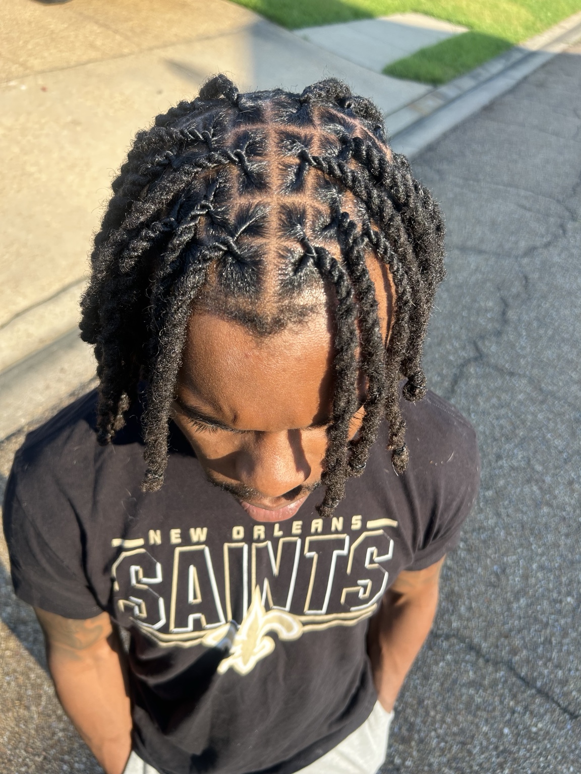 Looking down on a client's freshly retwisted locs outdoors, the parting grid crisp across the crown and the twisted lengths falling forward