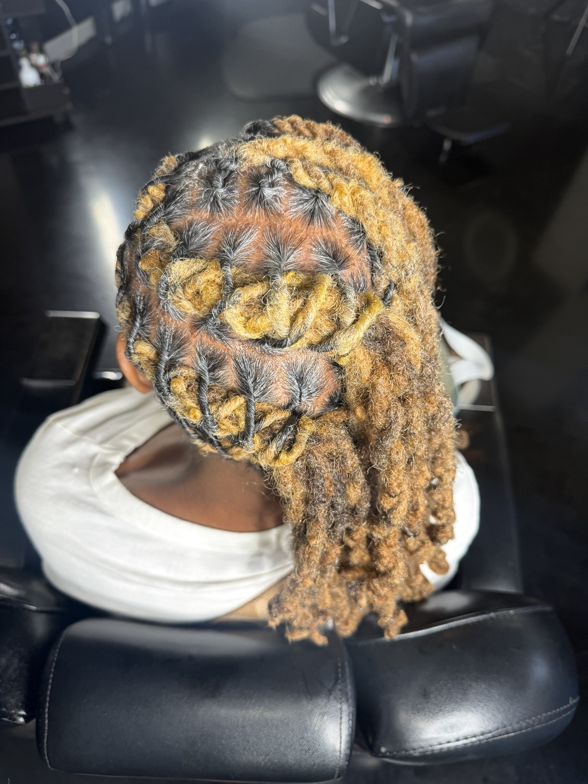 Crown view of honey-blonde locs freshly retwisted and set into soft barrel curls, parted in clean rows