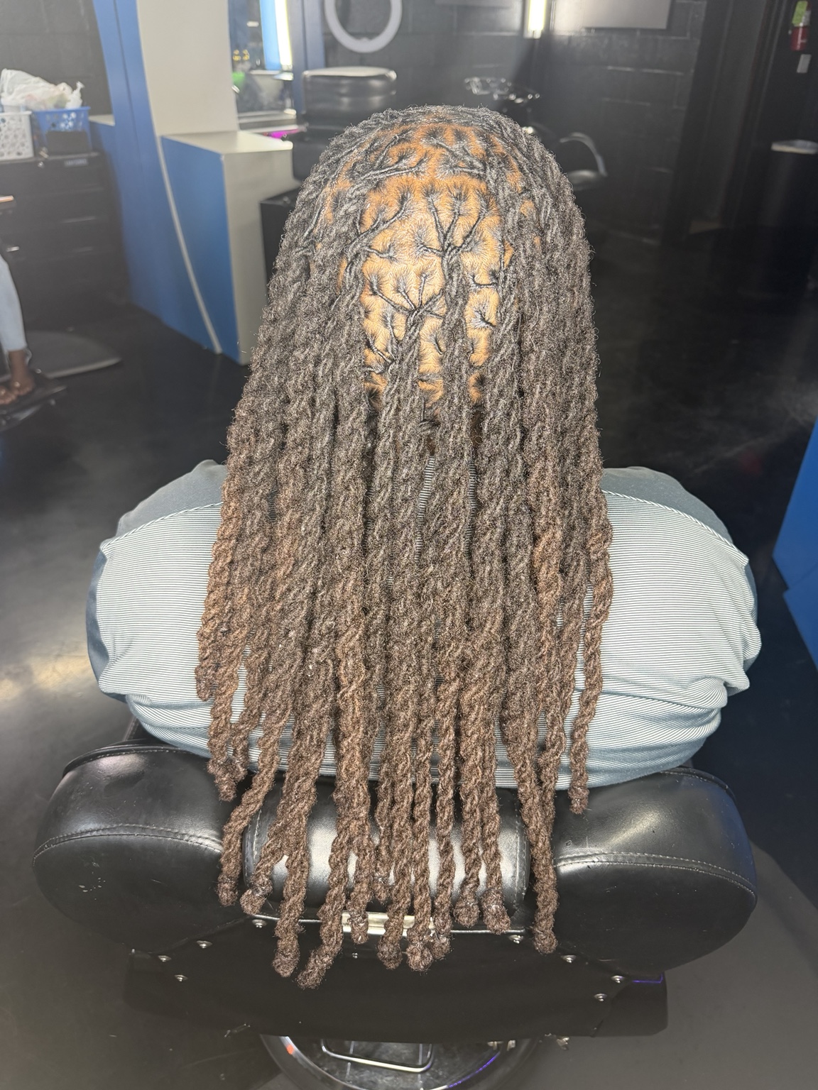 Client sitting in the salon chair after a full retwist, her locs falling in even parted rows the whole way down her back
