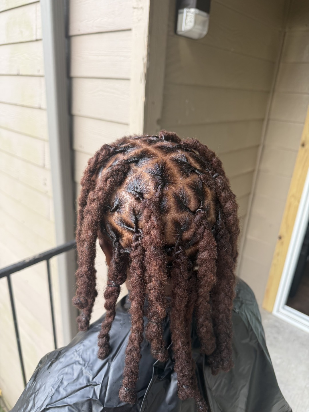 Finished retwist on copper-toned locs, the client still caped, every section parted and each end coiled