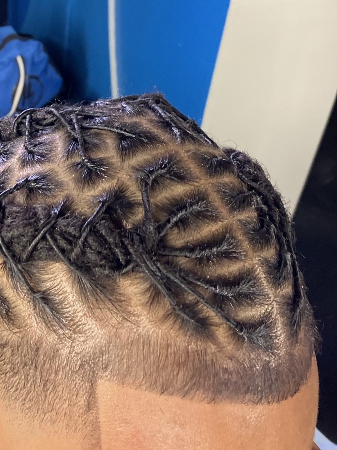 Close view of short locs freshly retwisted into a diamond parting pattern above a clean taper